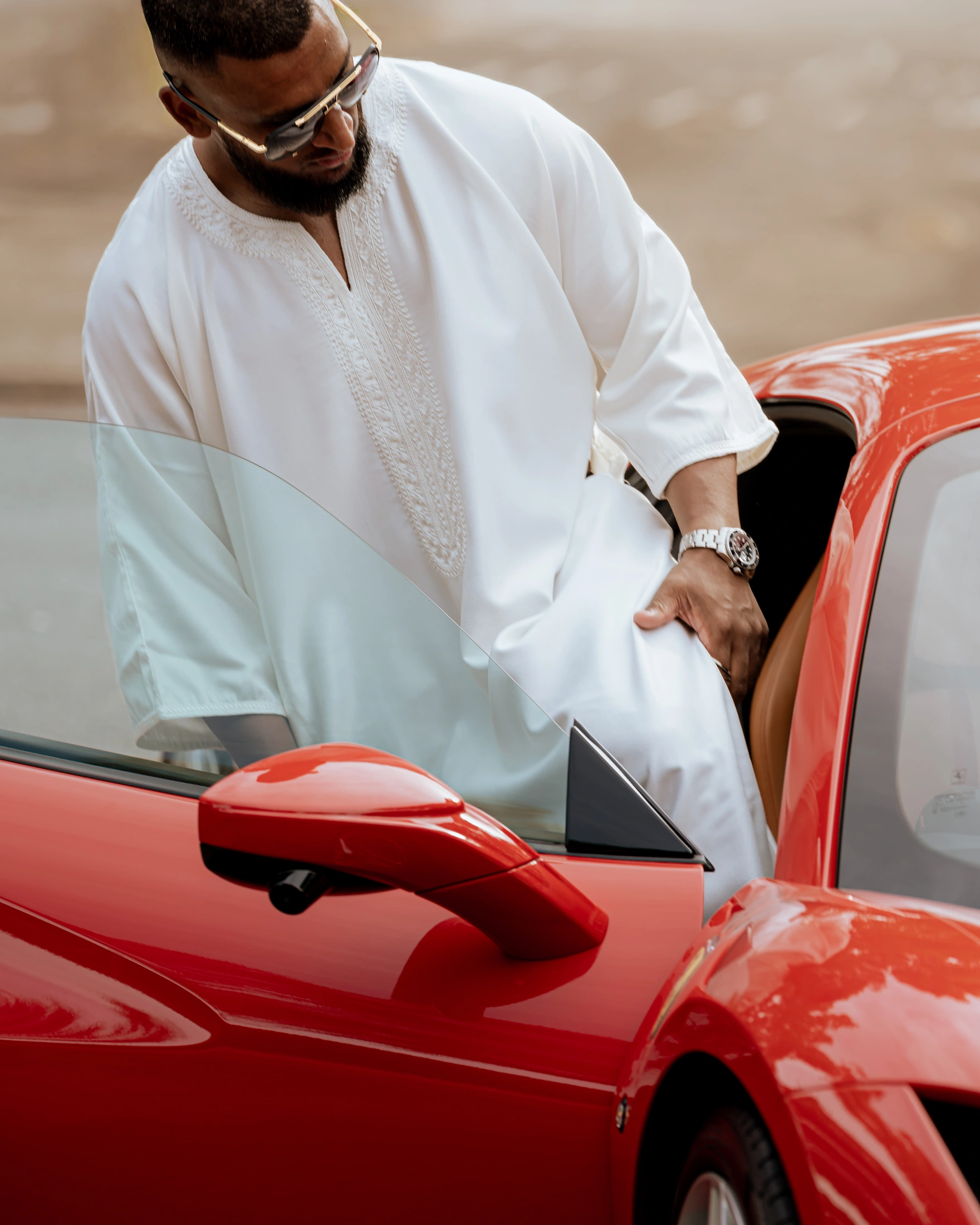 United Barakah white embroidered clothing beside a red Ferrari